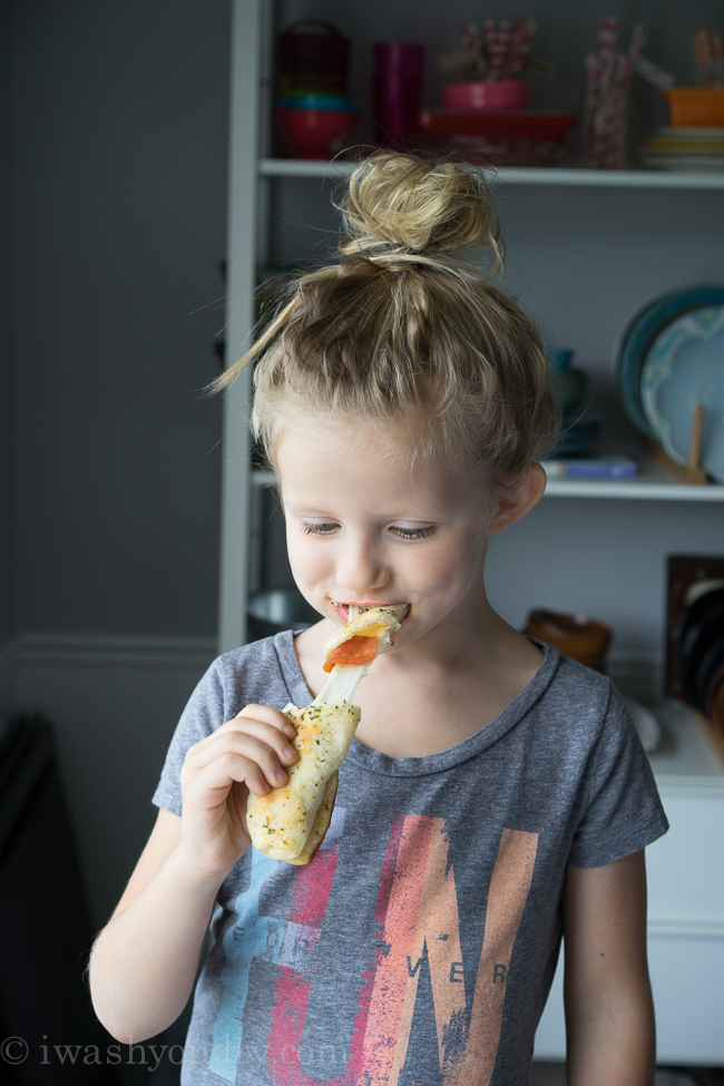 child biting pizza stick with gray shirt.