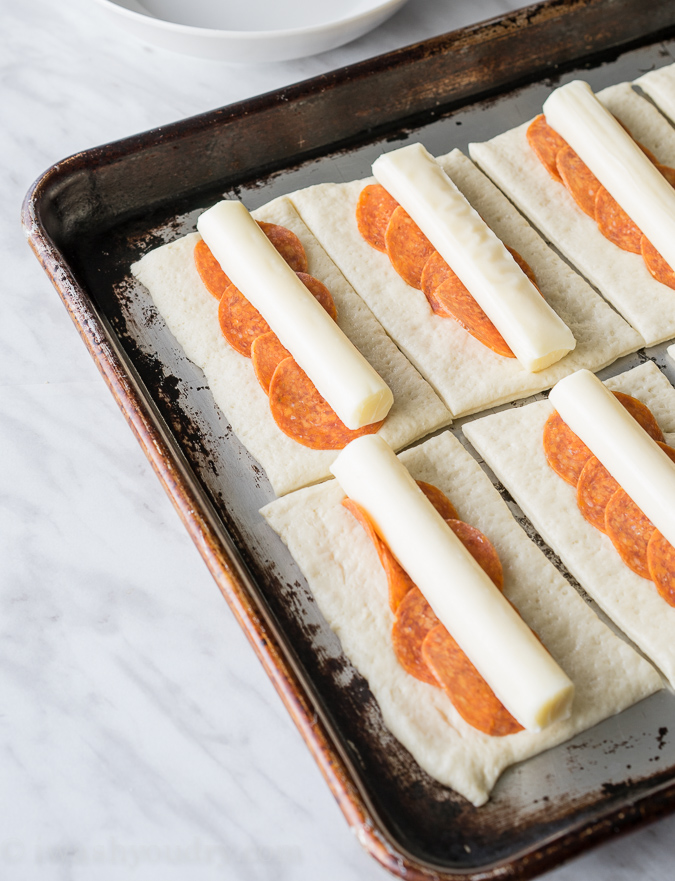 pizza dough with pepperoni and cheese sticks.