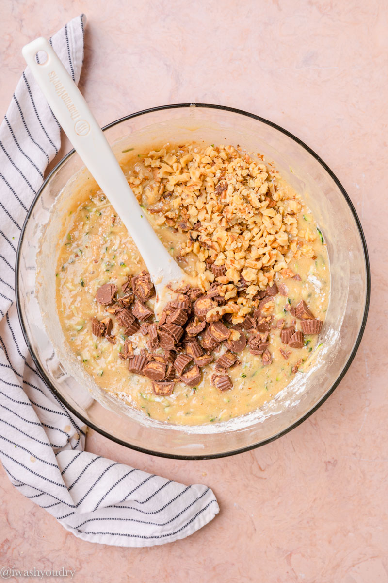 Chopped peanut butter cups and walnuts in zucchini bread batter in clear bowl. 