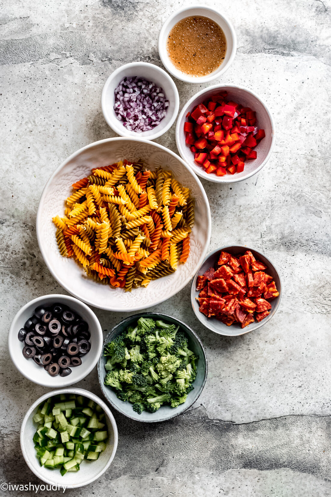 ingredients for italian pasta salad on white surface in small bowls.