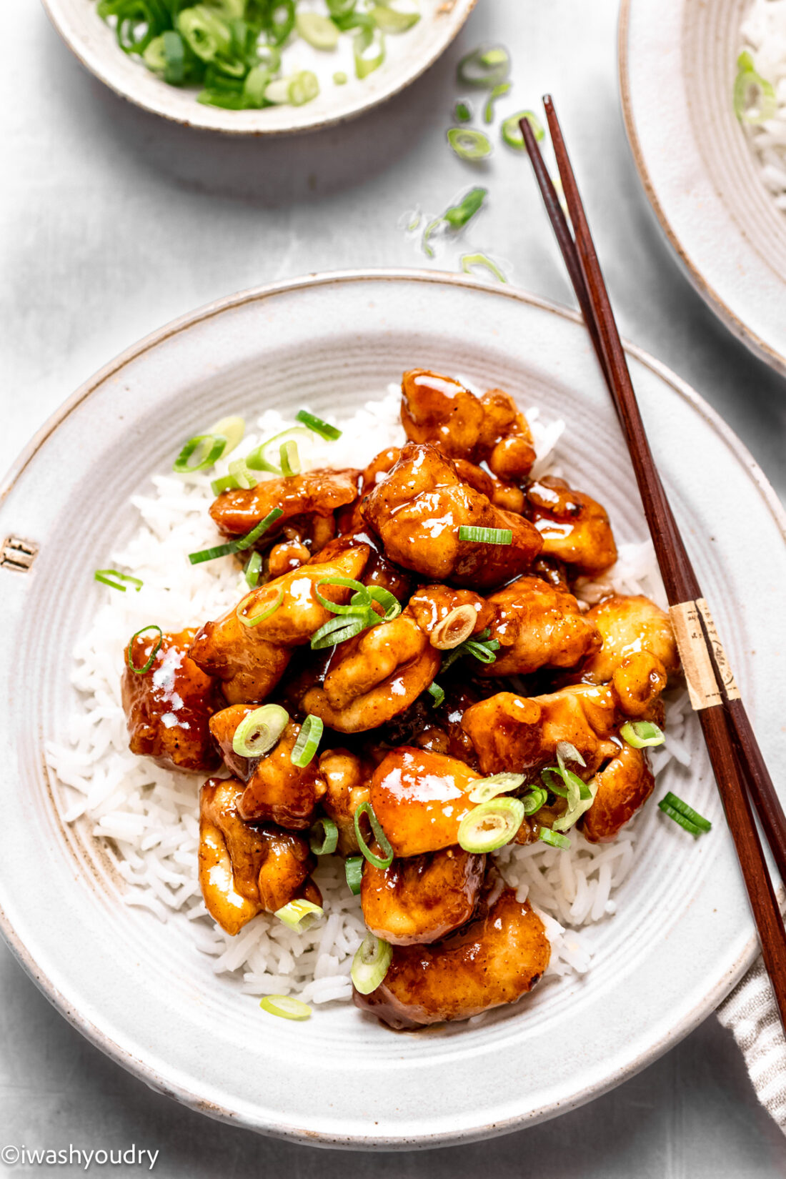 Cooked chicken on a bed of rice with chopsticks on a white plate. 