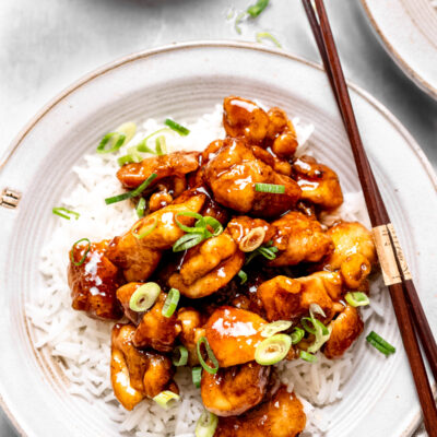 Cooked chicken on a bed of rice with chopsticks on a white plate.