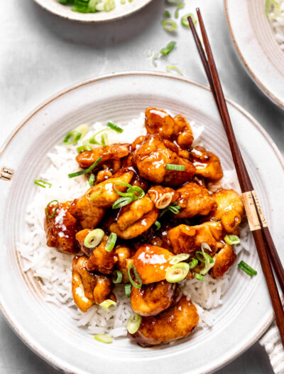 Cooked chicken on a bed of rice with chopsticks on a white plate.