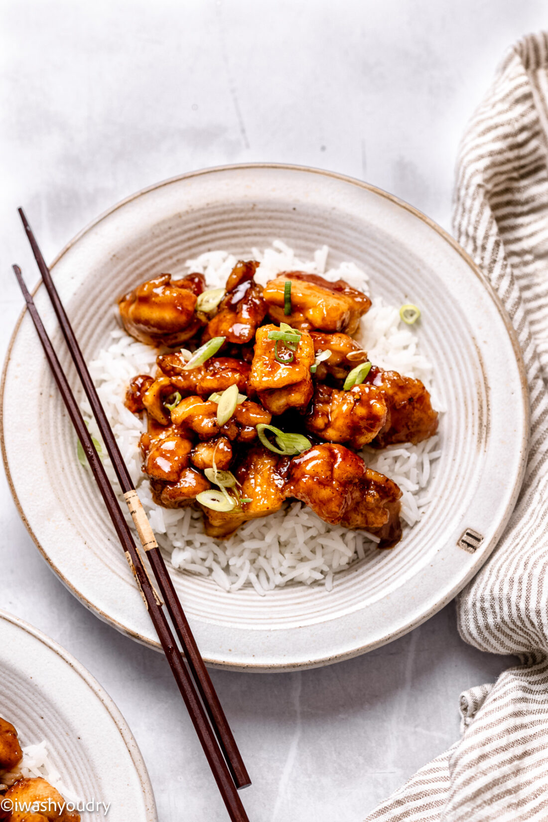 Cooked general tso's chicken on white plate with chopsticks and rice. 