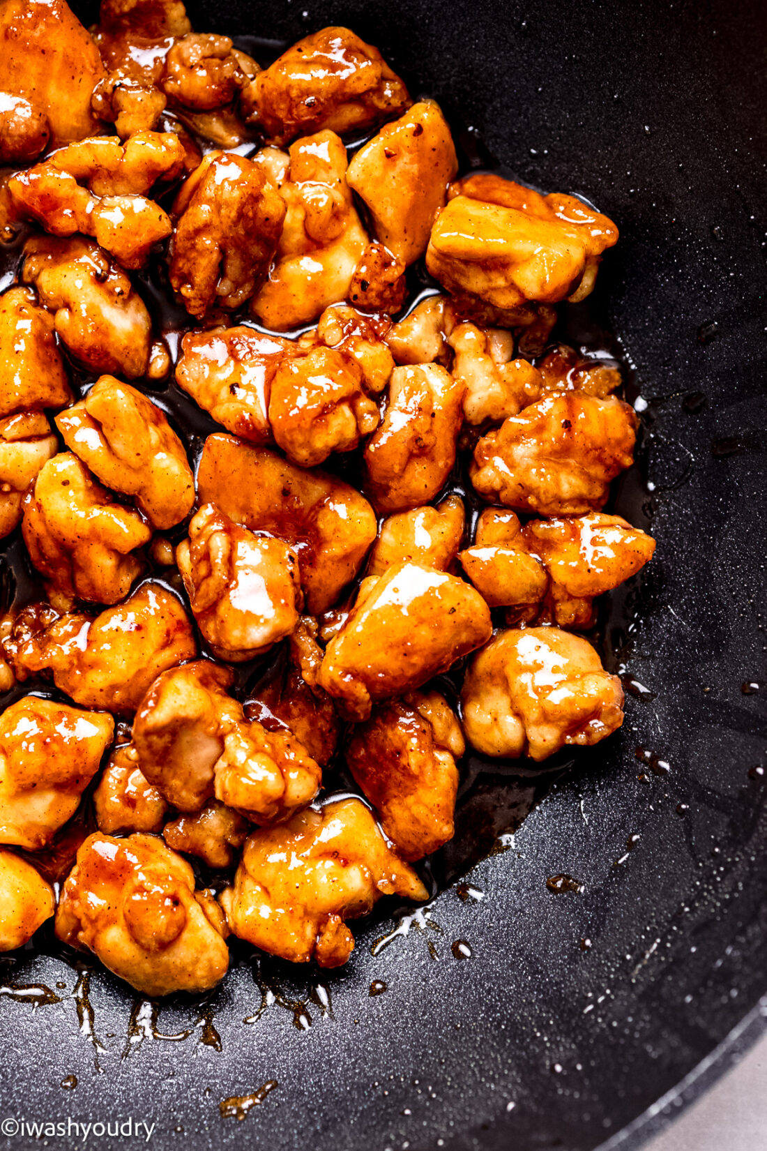 Cooked crispy chicken in sauce in black pan. 