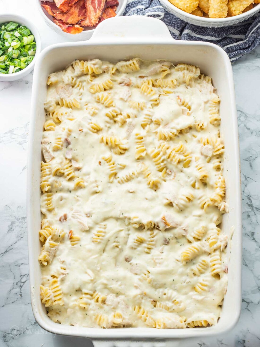 Unbaked chicken tater tot casserole in white casserole dish. 