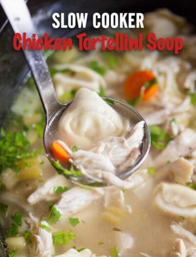 Close up of a spoon above a bowl of soup with chicken, noodles and veggies.