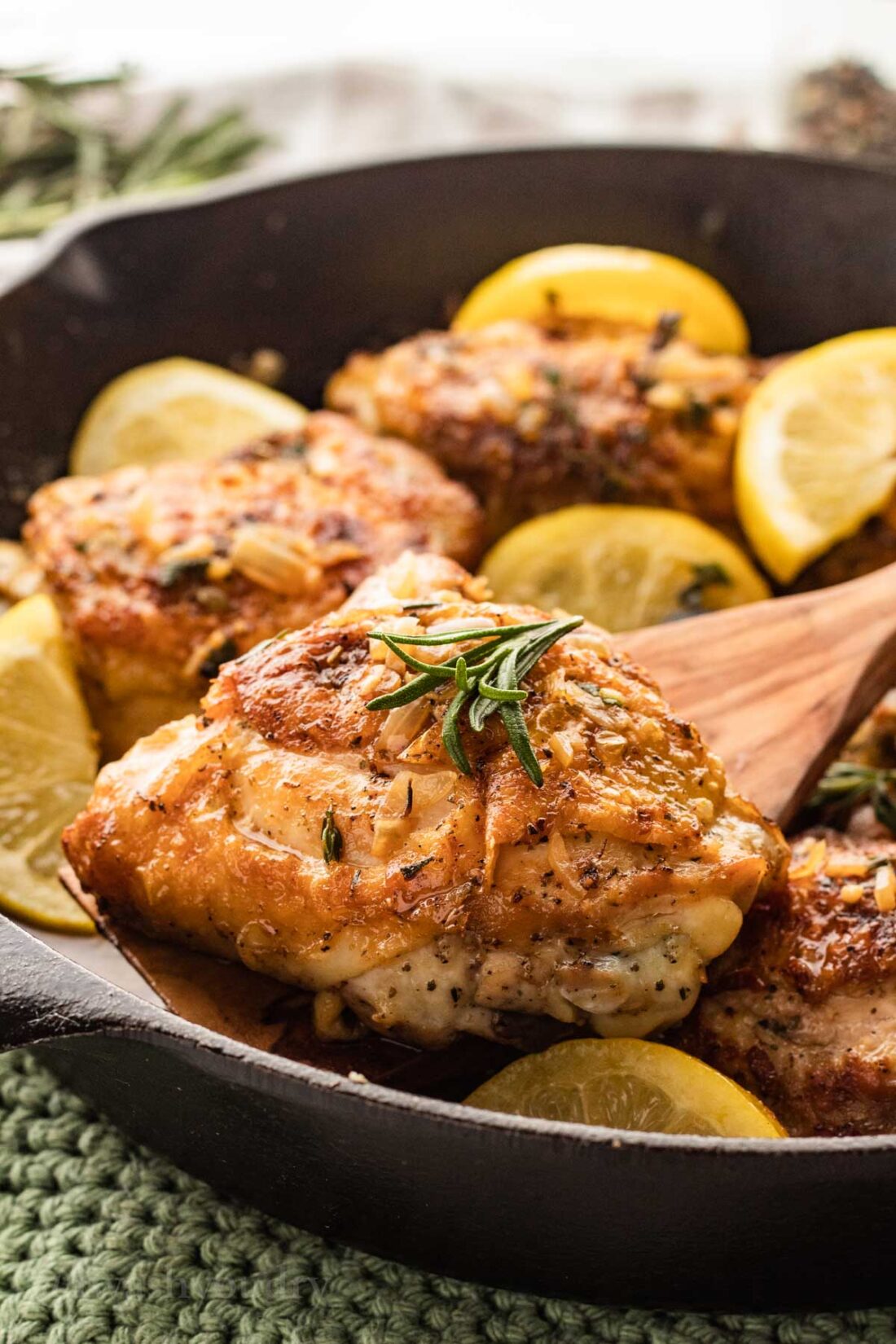 chicken thigh with crispy skin on a wooden spoon over black skillet.