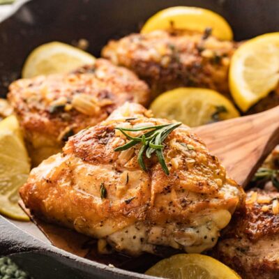 chicken thigh with crispy skin on a wooden spoon over black skillet.