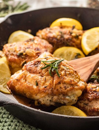 chicken thigh with crispy skin on a wooden spoon over black skillet.