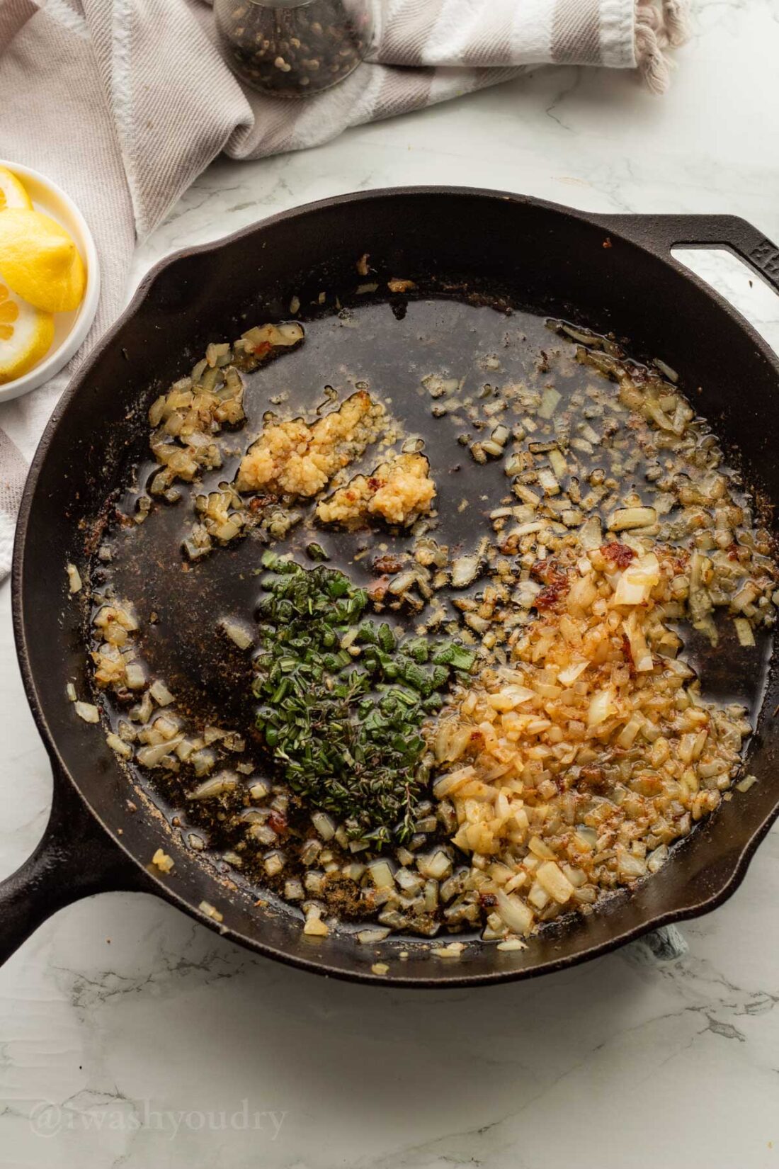 Herbs and onions added to black skillet.