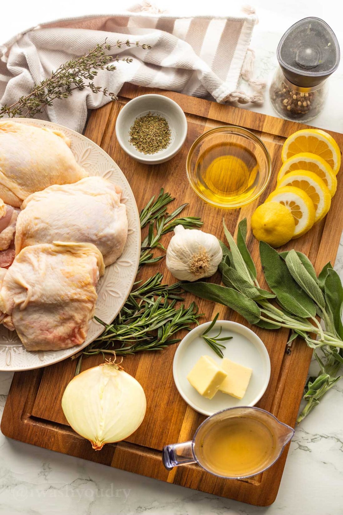 Ingredients for chicken thigh recipe on wooden surface with fresh herbs and lemons.