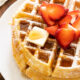 Crispy waffles on white plate with syrup and strawberries.