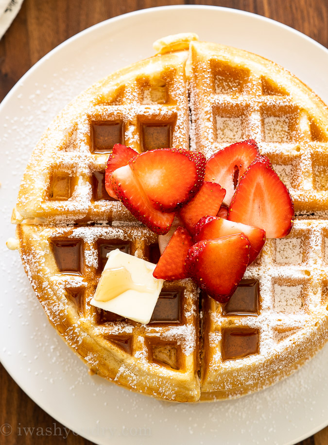 Large waffle on plate with butter and syrup and strawberries.