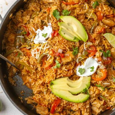 large black skillet filled with fajita rice, chicken and peppers. Topped with cheese and avocado slices.