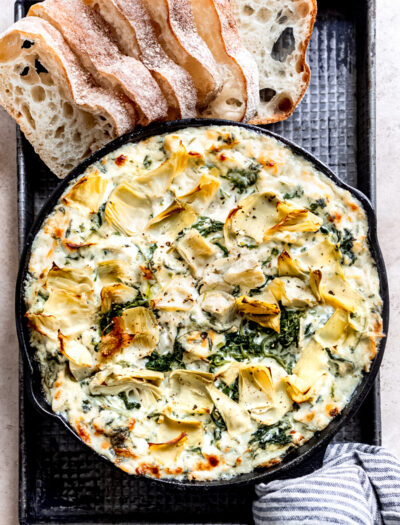 Black pan of spinach artichoke dip with bread on side.