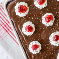 A close up of a pan of chocolate cake topped with frosting and cherries