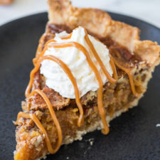 A slice of pecan pie on a plate topped with whipped cream and caramel sauce