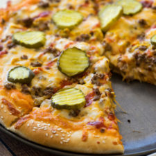 A pizza sitting on top of a pan, topped with cheese, veggies, meat and pickle slices