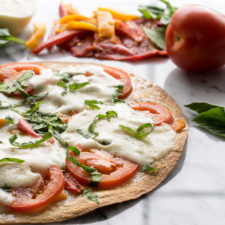 A close up of a baked tortilla with tomatoes, red peppers and melted cheese