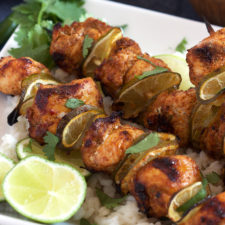 A plate with chicken chunks and lime slices on a skewers