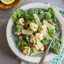 A bowl of salad, with spinach, noodles, sauce and veggies