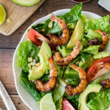 A bowl of salad with grilled shrimp, sliced tomatoes and sliced avocados