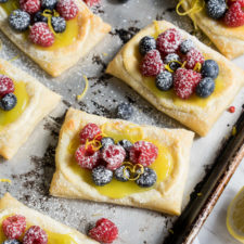 A close up of pastries on a pan topped with a lemon sauce and berries