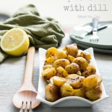 A serving bowl displayed on a table full of Pan Roasted Lemon Potatoes with dill.