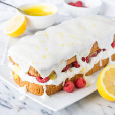 A loaf of pound cake on a plate on a table, with white frosting and an exposed center of lemon raspberry filling