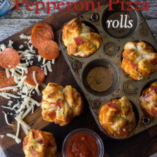 Looking down on a cupcake pan of rolls with a couple removed and beside the pan with red sauce, shredded cheese and pepperoni slices