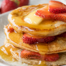 Stacked pancakes on a plate, with strawberries and topped with butter and syrup