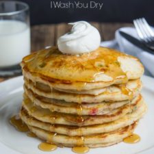 A stack of pancakes on a plate topped syrup and whipped cream