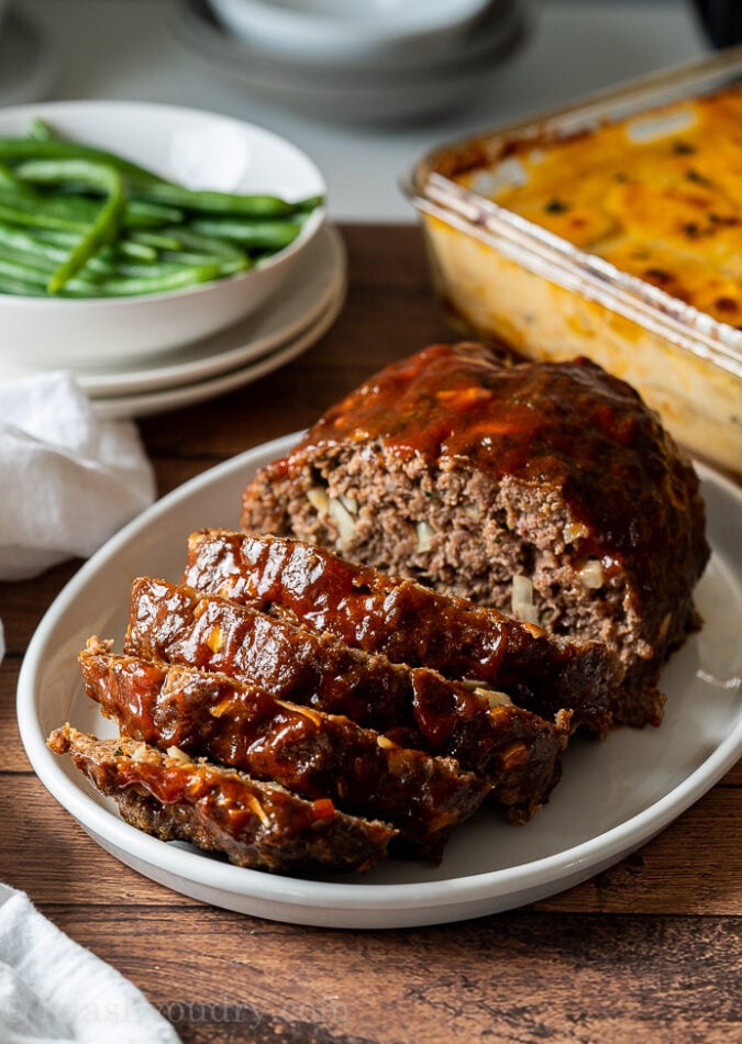 Sliced meatloaf on white platter, covered in meatloaf glaze.