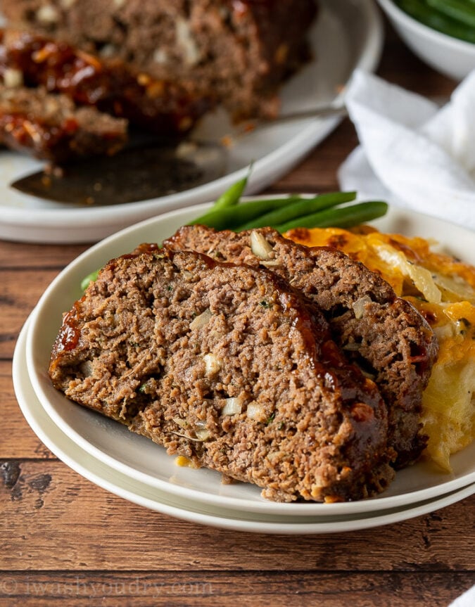 Sliced meatloaf on white plate with green beans and potatoes.