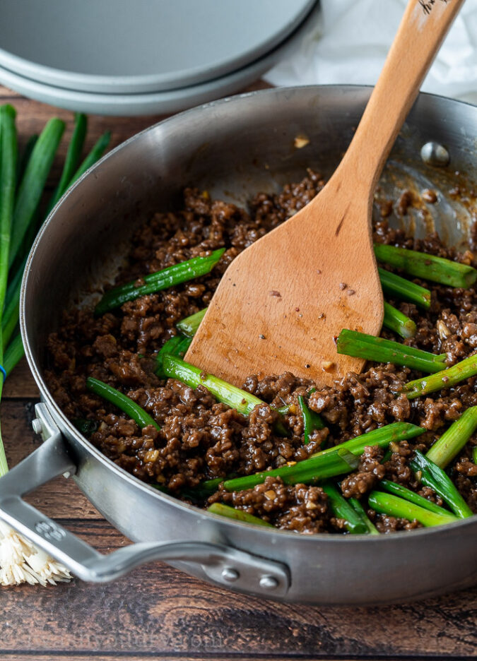 browned hamburger in pan with wooden spoon and green onions.