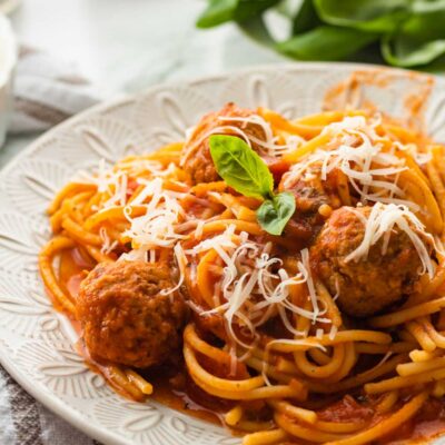 Cooked spaghetti with sauce and meatballs on white plate.