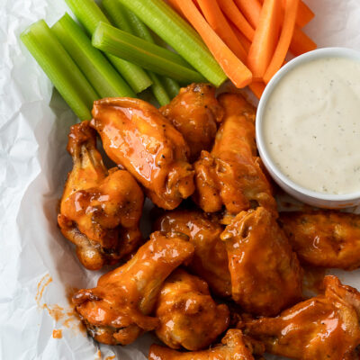 Saucy Buffalo Wings in basket with celery and carrots and a side of ranch dressing