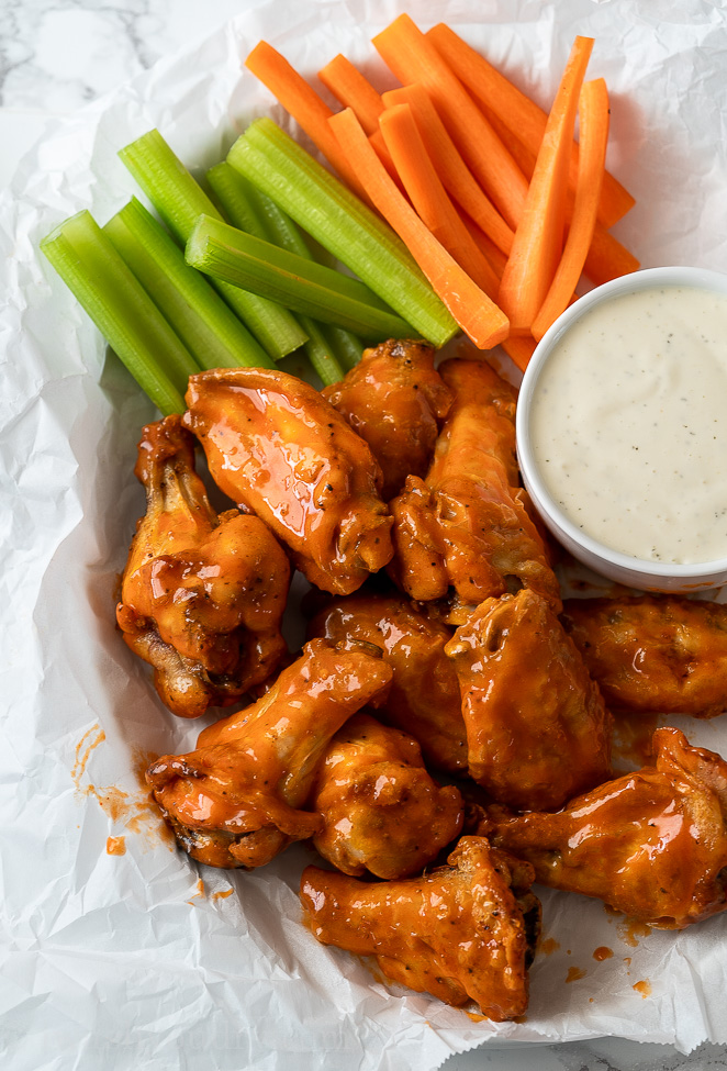 Saucy Buffalo Wings in basket with celery and carrots and a side of ranch dressing