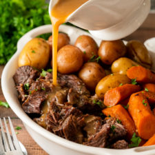 Pouring gravy over shredded beef pot roast in white dish.