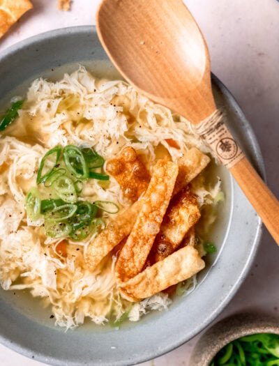 Cooked egg drop soup in gray bowl with wooden spoon.