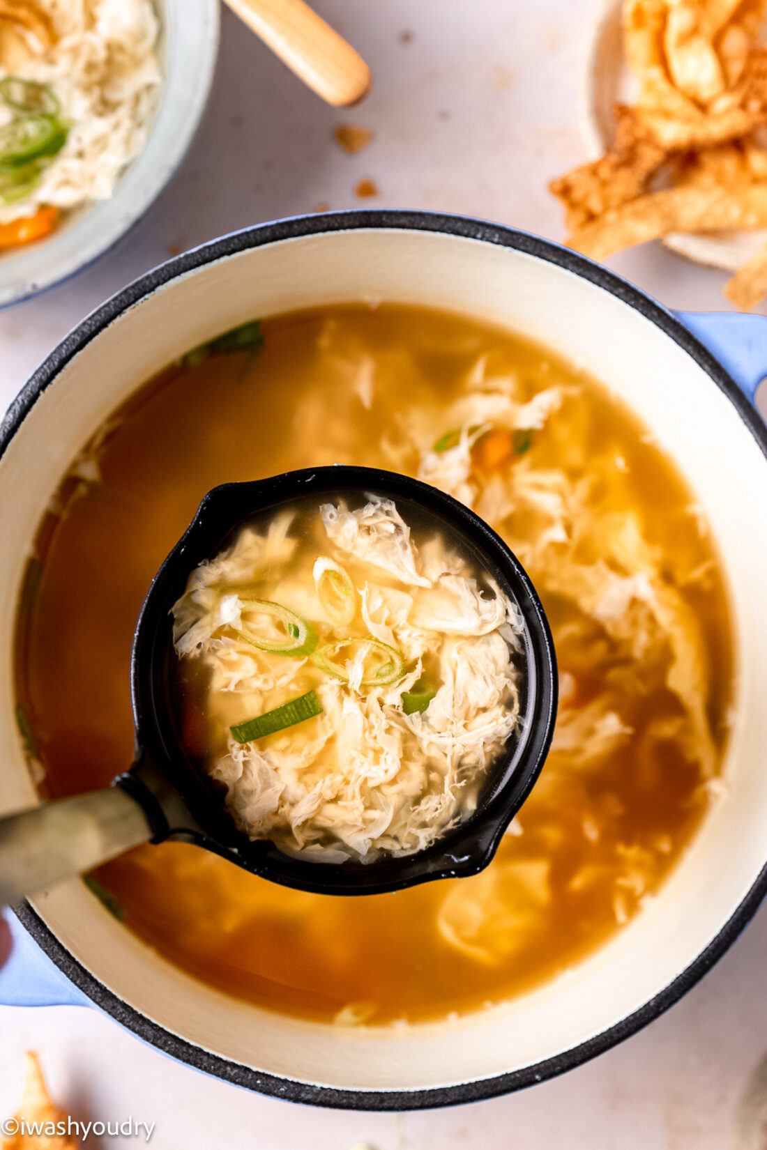 Ladle of cooked egg drop soup above pan. 