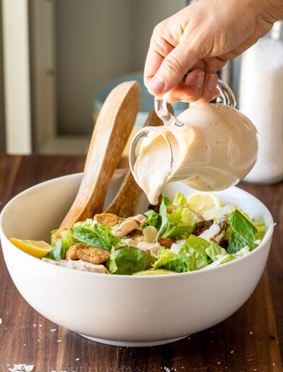 Homemade Caesar Salad Dressing being poured over chopped lettuce.