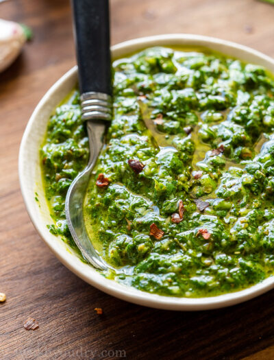 Small white bowl filled with green chimichurri sauce and red pepper flakes.