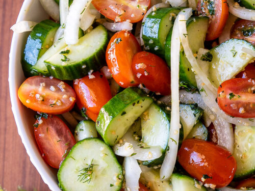 White bowl filled with cool cucumbers, tomatoes and sliced onions