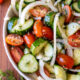 White bowl filled with cool cucumbers, tomatoes and sliced onions