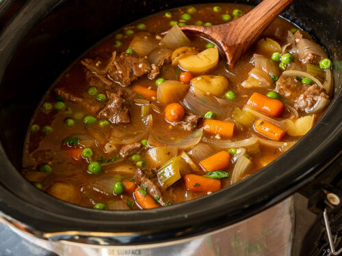 Beef stew in a slow cooker with wooden spoon