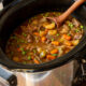 Beef stew in a slow cooker with wooden spoon