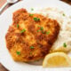 pork schnitzel on top of mashed potatoes with lemon wedge.