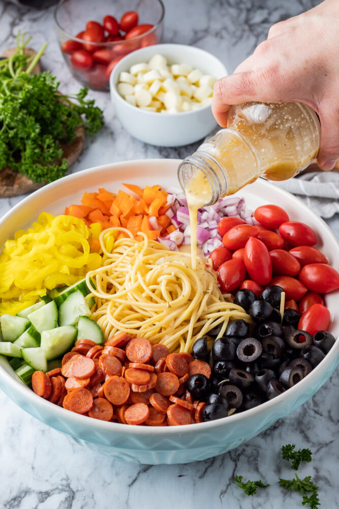 Italian dressing pouring into bowl of spaghetti and veggies. 